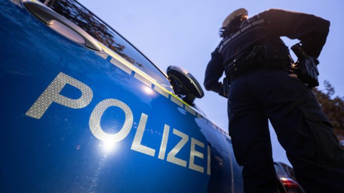 Polizei - Symbolbild Ein Polizist steht bei einem Einsatz neben einem Streifenwagen.