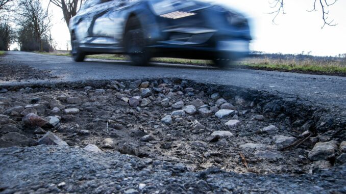 Auto fährt an einem Schlagloch vorbei Die Reparaturen an den Schlaglöchern auf Hamburgs Straßen haben begonnen. (Symbolfoto).