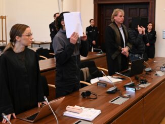 Die Angeklagten halten sich vor Beginn des Prozesstages Dokumente vor das Gesicht.