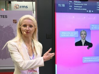 HVV-Geschäftsführerin Anna-Theresa Korbutt zeigt auf einen Sprachassistenten mit ihrem eigenen Gesicht.